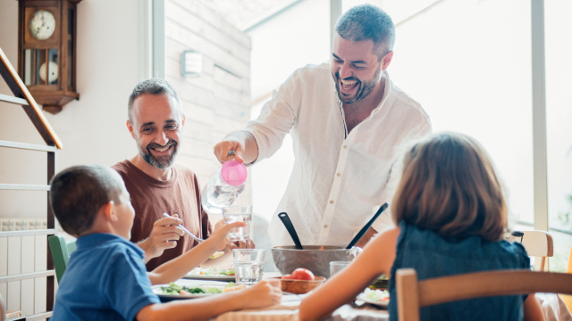 Two male parents enjoy a meal with their adopted son and daughter.