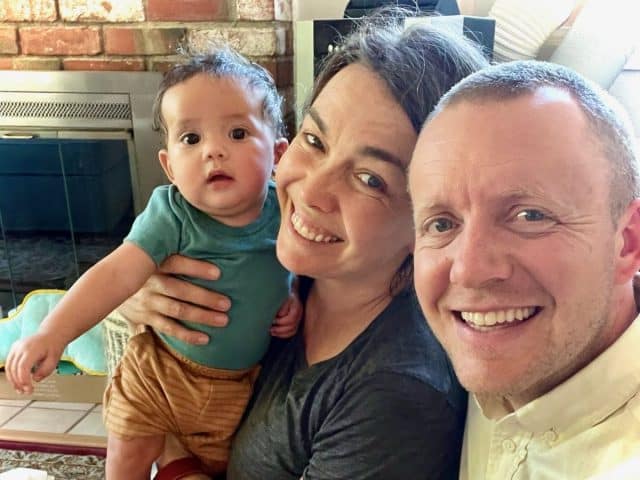 Two parents pose smiling with their adopted baby. 